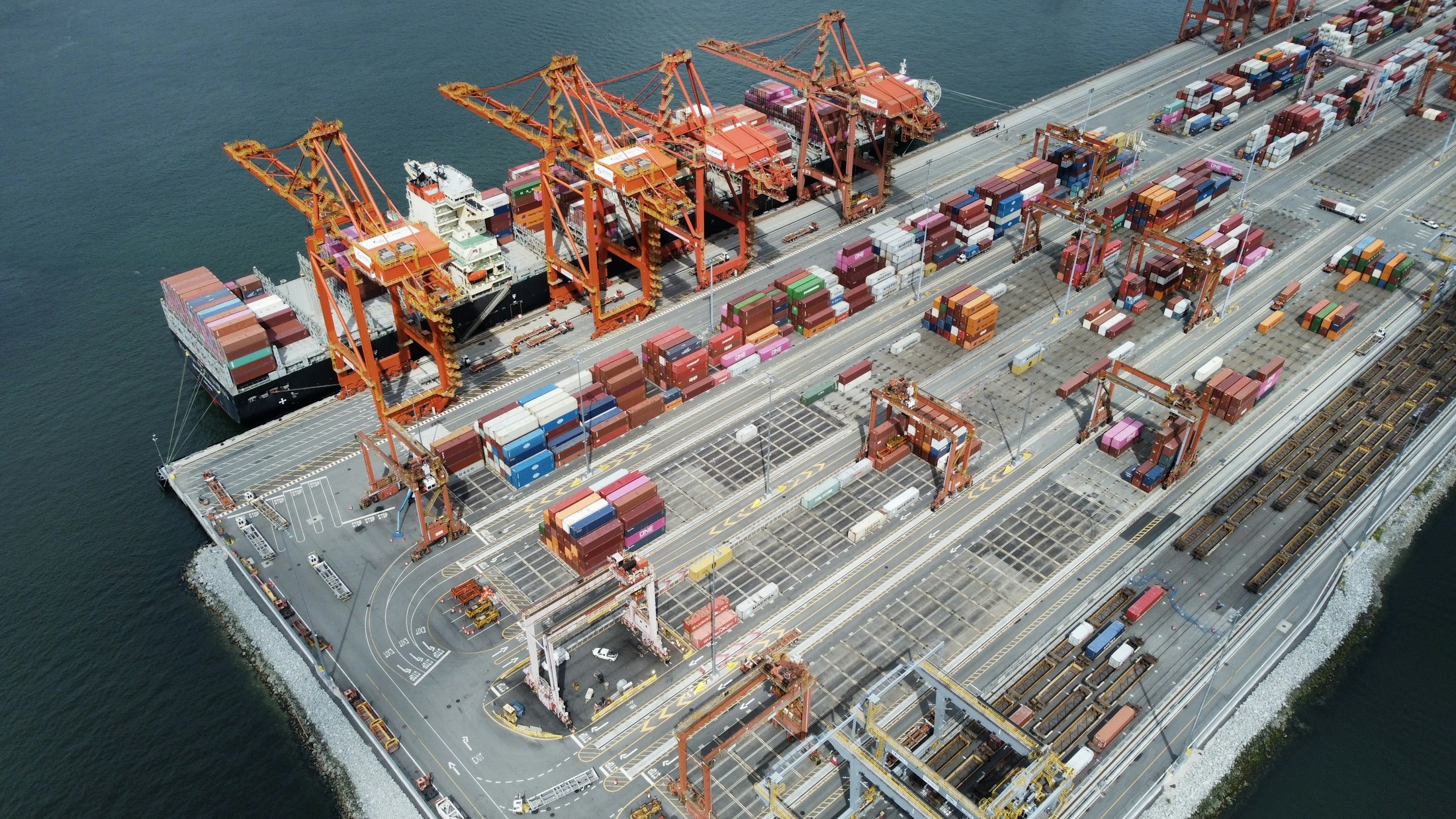 Vue aérienne d’un terminal portuaire, avec un navire à quai, des grues et des voies de circulation entre les conteneurs